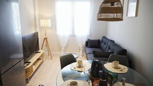 Ein modernes Wohnzimmer mit Fernseher, Sofa, Esstisch und einer hängenden Lampenschirm aus Korbgeflecht.