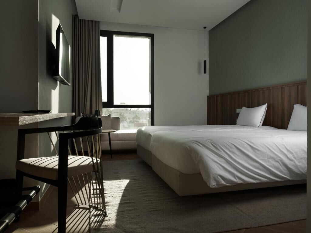 A hotel room with a bed, a desk, a chair, a TV, and a window.
