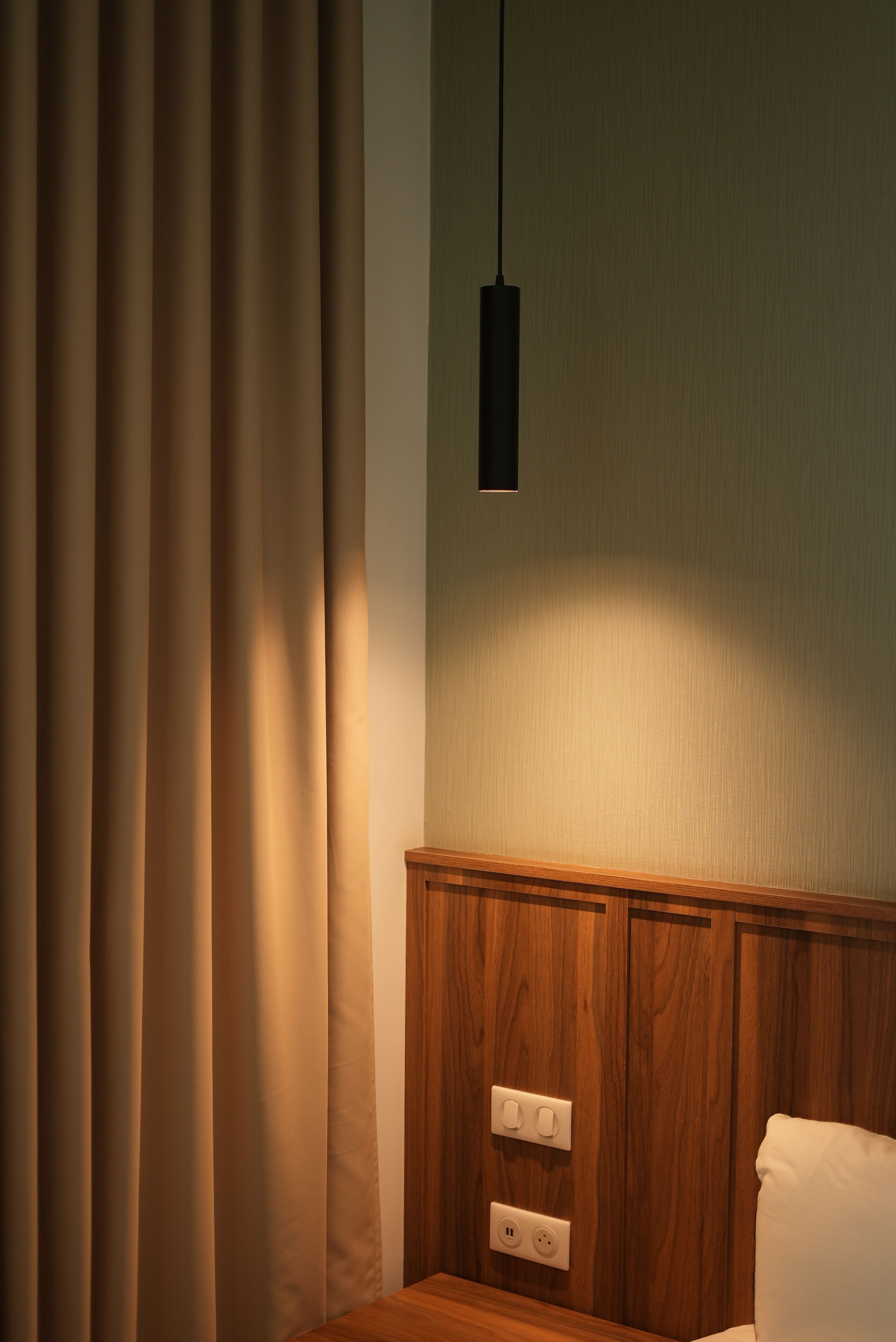 Una habitación con pared de paneles de madera, una lámpara colgante y una cama con almohada blanca.