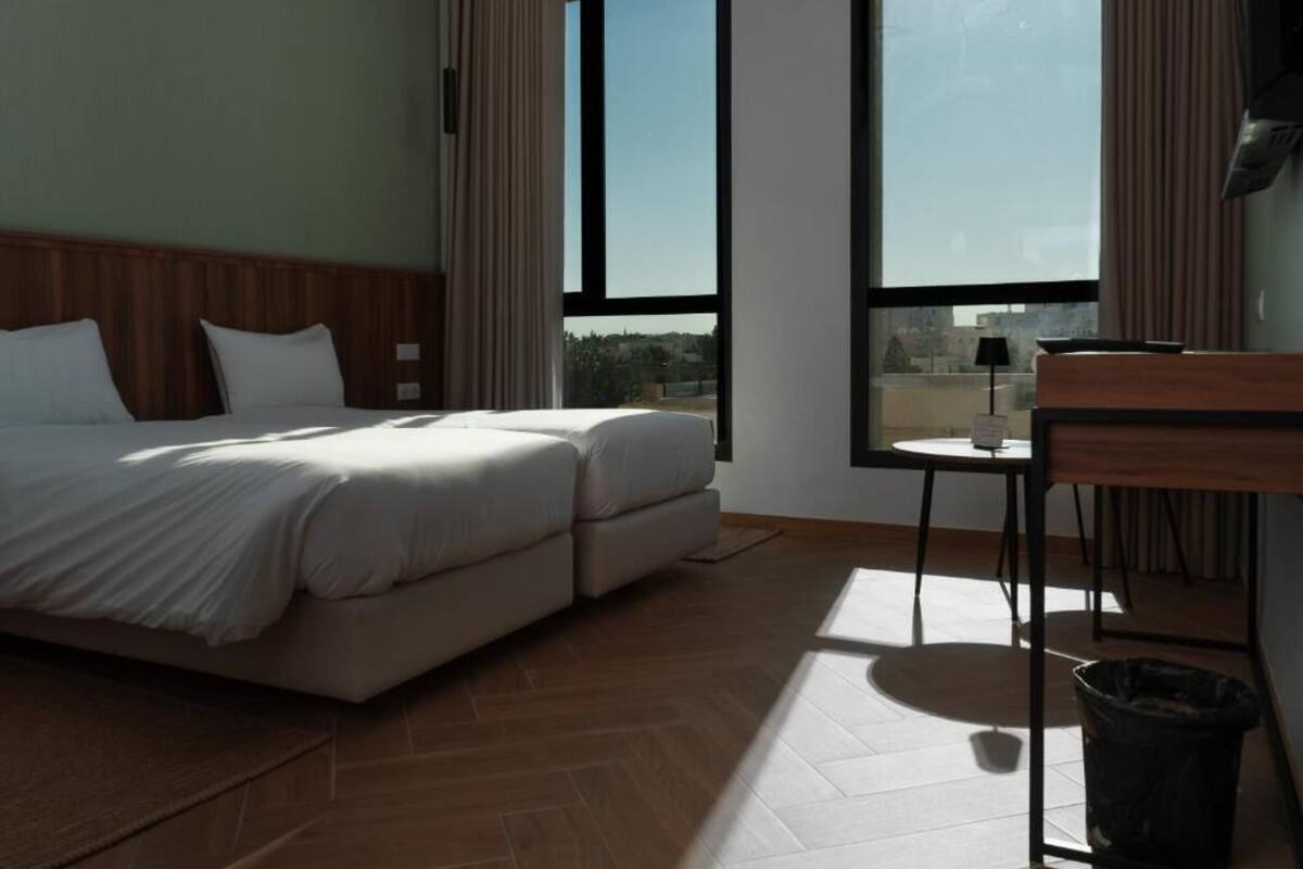 Habitación de hotel con cama, escritorio y ventanas grandes.