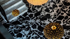 Una escalera con piso de mármol blanco y negro, un gran lámpara esférica dorada y luces esféricas doradas más pequeñas.