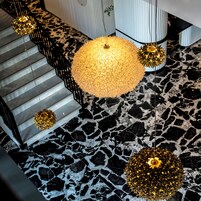 Una escalera con piso de mármol blanco y negro, un gran lámpara esférica dorada y luces esféricas doradas más pequeñas.