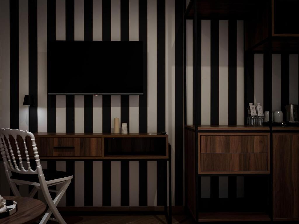 A modern room with a flat-screen TV mounted on a wall with black and white stripes, a wooden chair, and a wooden cabinet with drawers.