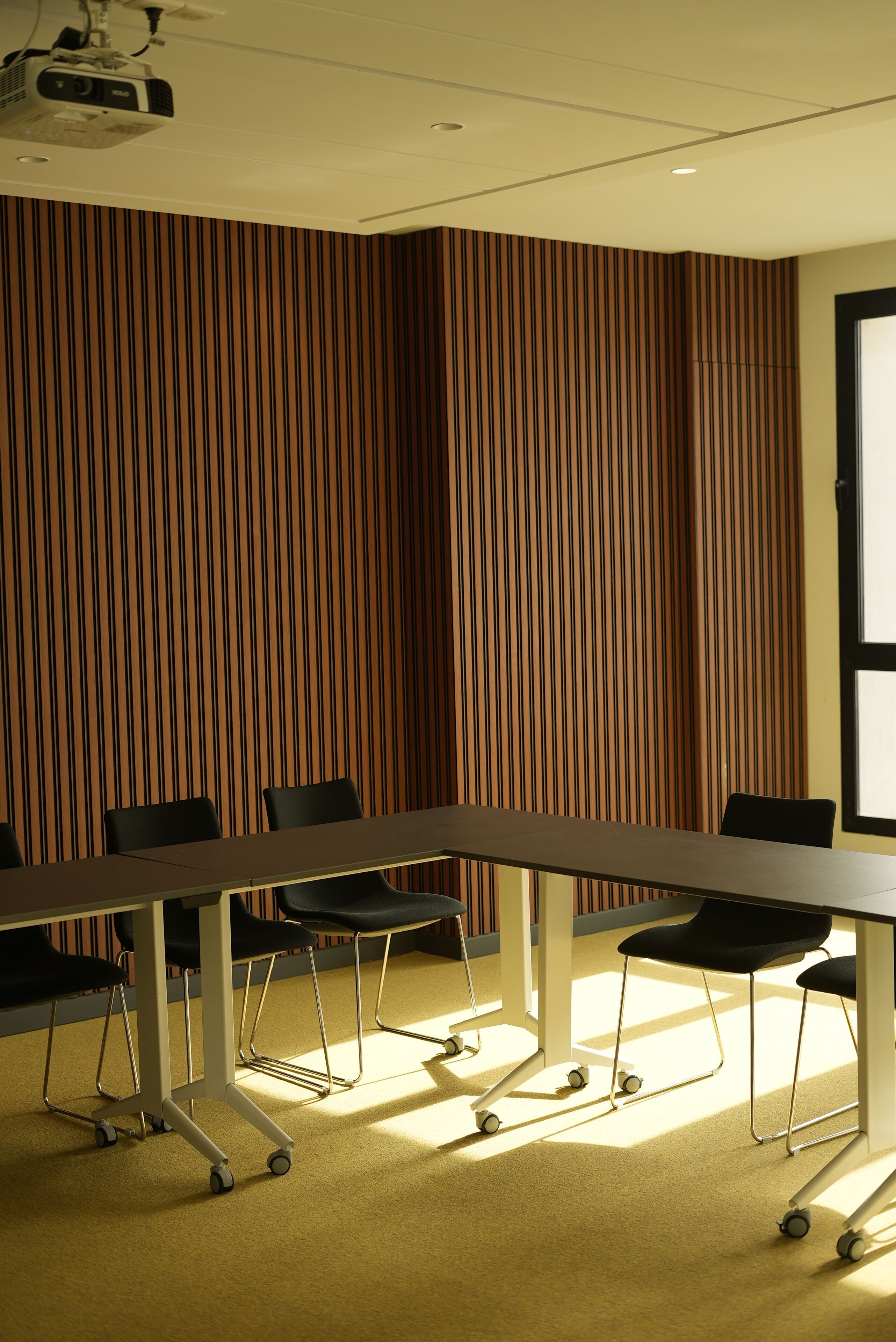 A conference room with a long table, four chairs, and a projector on the ceiling.