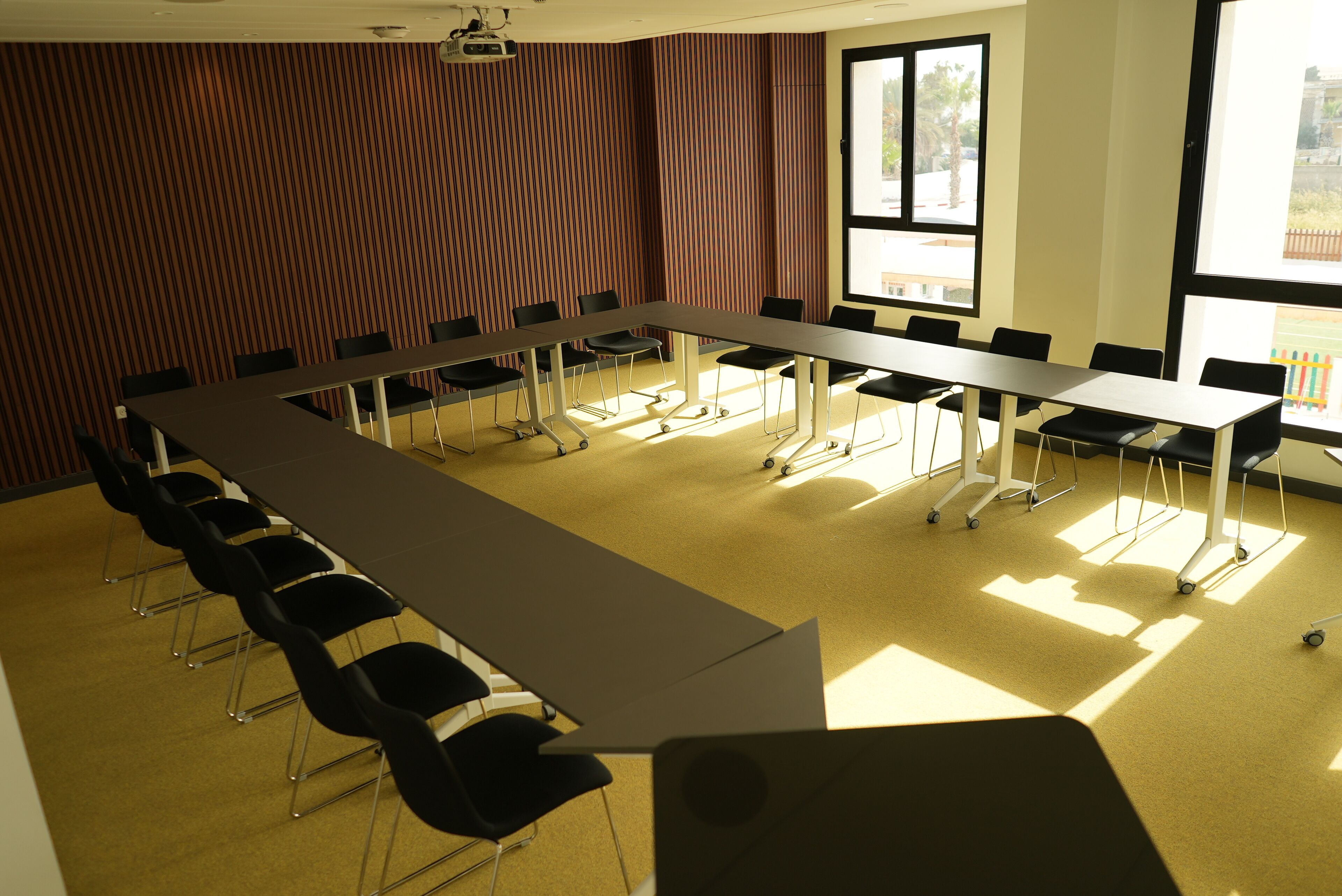 Een vergaderruimte met een lange tafel, stoelen, grote ramen en een gestreepte wand.