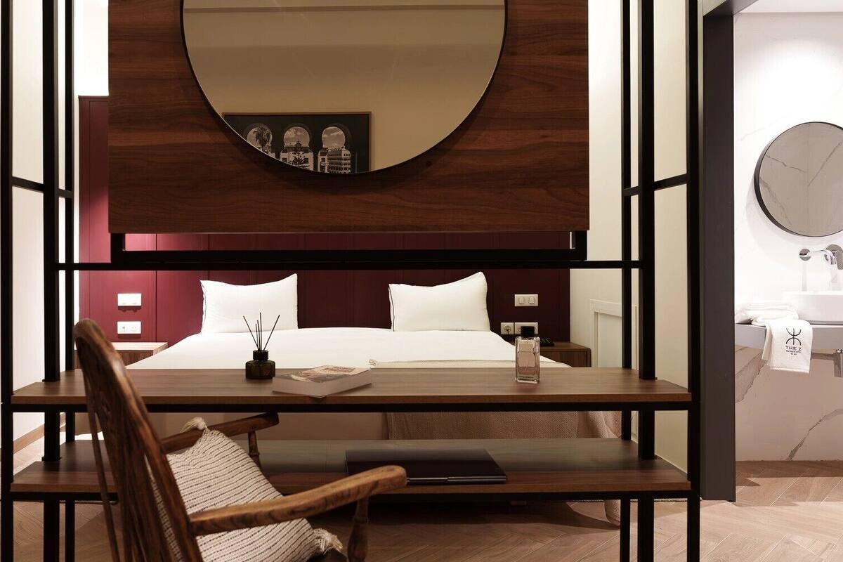 Una habitación de hotel con cama, mesita de noche, silla y un espejo grande.