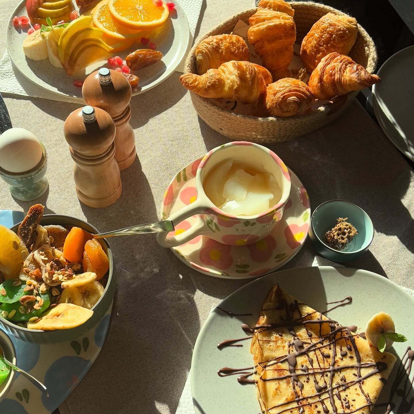 Une table dressée pour le petit-déjeuner avec des croissants, des fruits et un gaufre nappé de chocolat.