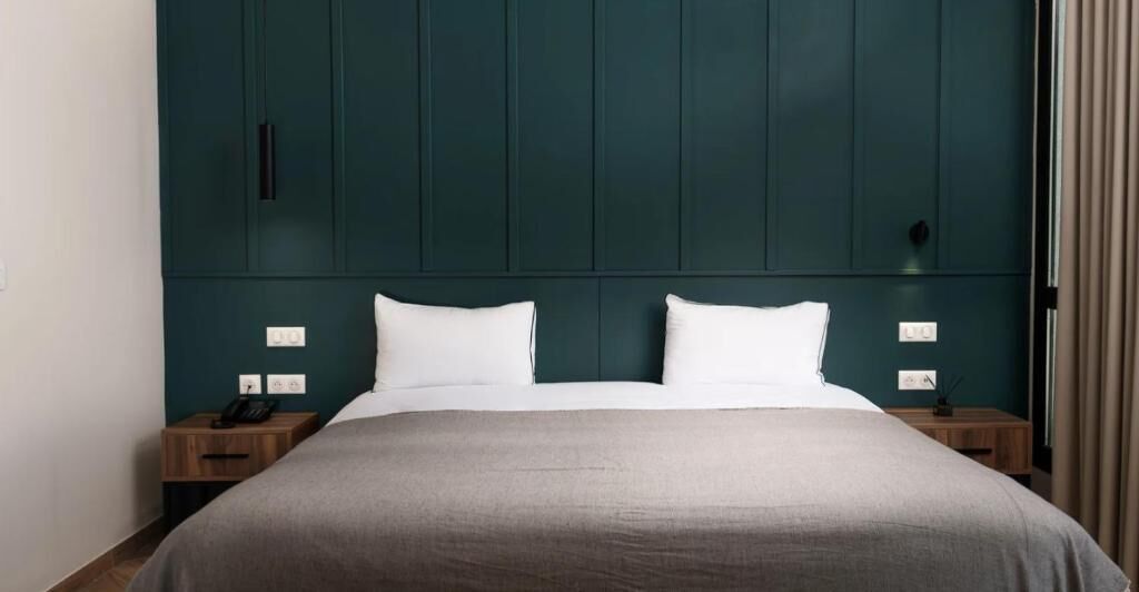A hotel room with a large bed, two bedside tables, and a dark green headboard.