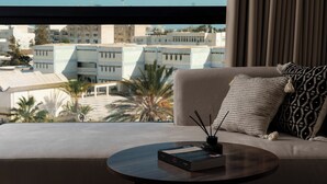 Una sala de estar moderna con un sofá, una mesa de centro redonda y vistas a un paisaje urbano a través de amplios ventanales.