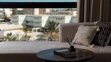 Una sala de estar moderna con un sofá, una mesa de centro redonda y vistas a un paisaje urbano a través de amplios ventanales.