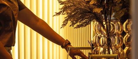 A person adjusting a water tap in a bathroom with a decorative vase of dried flowers on the counter.