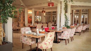 Ein Restaurant mit stuhl- und tischbestückten Sitzgelegenheiten mit floralem Muster, einer dekorativen Fontäne und hängenden Pflanzen.