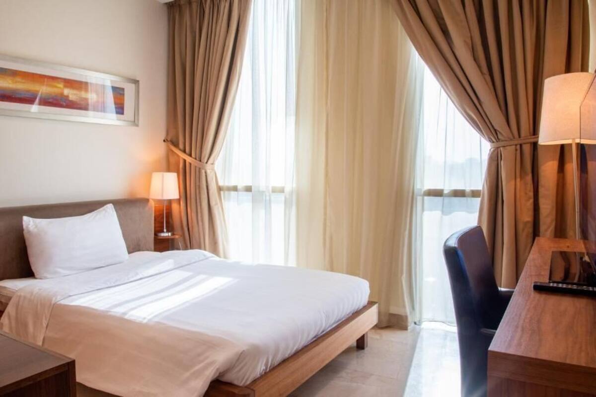 Une chambre d’hôtel avec un lit, des tables de chevet, un bureau, une chaise et des rideaux.