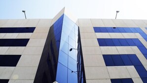 Ein modernes Gebäude mit einer glänzenden Glasfassade und einem geometrischen Muster aus hellen und dunklen Paneelen an der Außenwand.