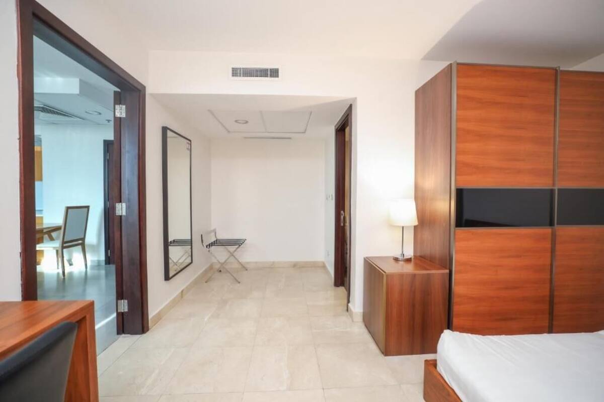 Une chambre d’hôtel avec un lit, une armoire en bois, une petite table avec une lampe, une chaise et un grand miroir.