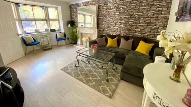 A living room with a stone wall, a sofa with yellow cushions, a coffee table, and a small table with a vase. - Charming Cottage Overlooking River & Nr Town /FREE Parking (Maidstone)