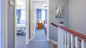 A hallway leading to a bedroom with a bed, a dresser, and a painting of the Eiffel Tower. - Charming Cottage Overlooking River & Nr Town /FREE Parking (Maidstone)