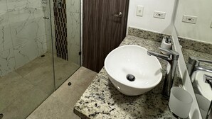 A modern bathroom with a glass shower enclosure, a marble-tiled wall, a wooden door, and a granite countertop with a sink and vanity. - Bright and Comfortable 2 Bedroom Apartment in Serena del Mar Cartagena (Cartagena)
