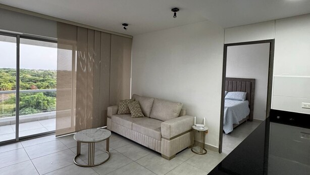A modern, well-lit living room with a sofa, a small round table, and a bed with a headboard. - Bright and Comfortable 2 Bedroom Apartment in Serena del Mar Cartagena (Cartagena)
