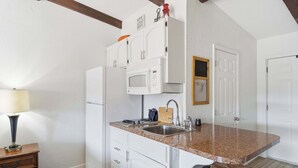A compact kitchen with white cabinets, a microwave, and a sink. - Driftwood Den – Condo for 2 (Kimberling City)