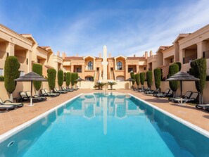 A pool area with lounge chairs and umbrellas, surrounded by buildings with a symmetrical architectural design. - Baia da Luz - Upper Luz Suite (Luz)