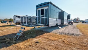 A mobile home with a large sliding door, a ladder, and a gravel driveway. - Family-Friendly Luxury RV Retreat/Fire Pits/Fishing Pond/Boat Tours. (Princeton)