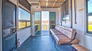A train carriage with a bench seating area, large windows, and a fire extinguisher. - Family-Friendly Luxury RV Retreat/Fire Pits/Fishing Pond/Boat Tours. (Princeton)
