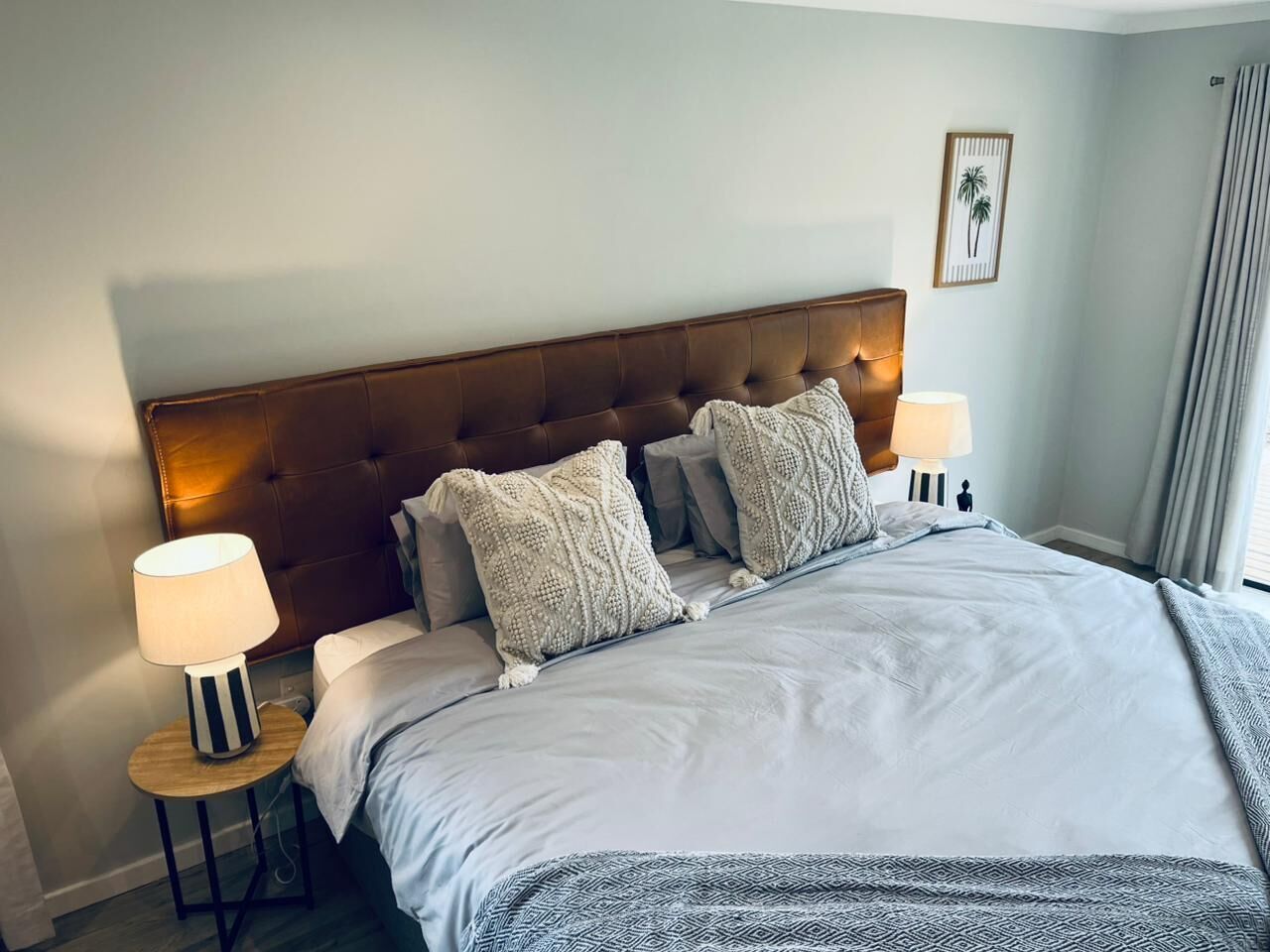 A neatly made bed with a tufted headboard, two bedside lamps, and a framed picture on the wall.