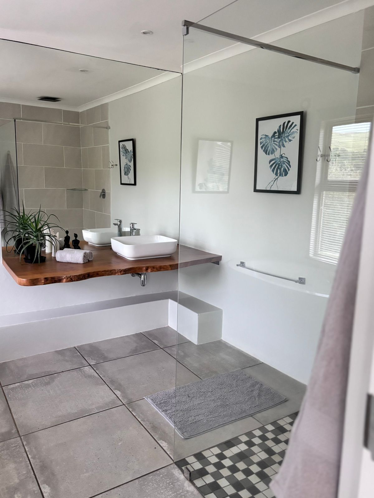 A modern bathroom with a glass shower enclosure, a wooden vanity, a white sink, and a large mirror.