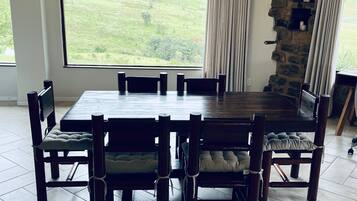 A dining area with a large table and chairs, a stone wall, and a view of a green landscape.
