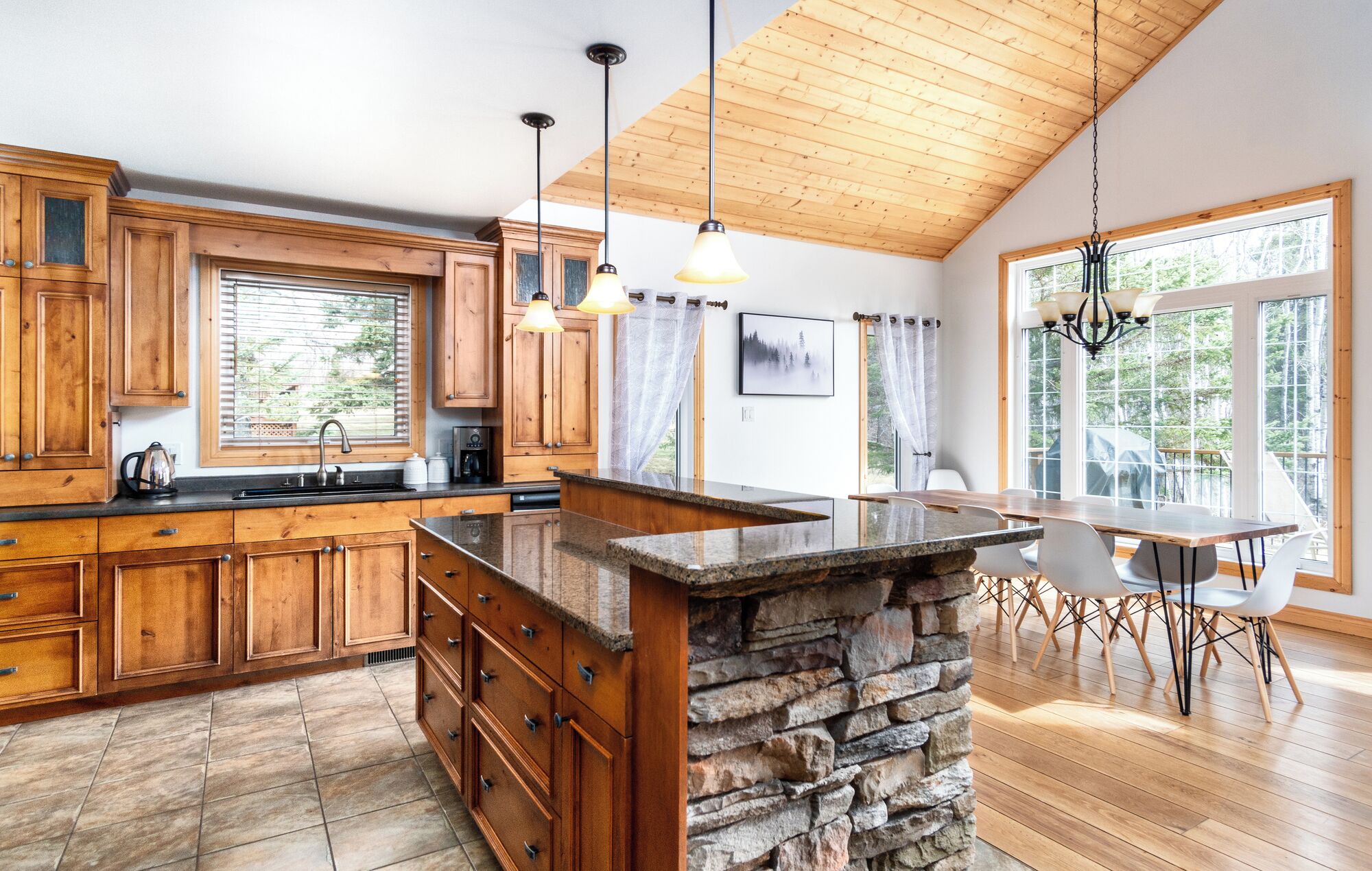 A spacious kitchen with wooden cabinets, a granite island, and a dining area with a table and chairs.