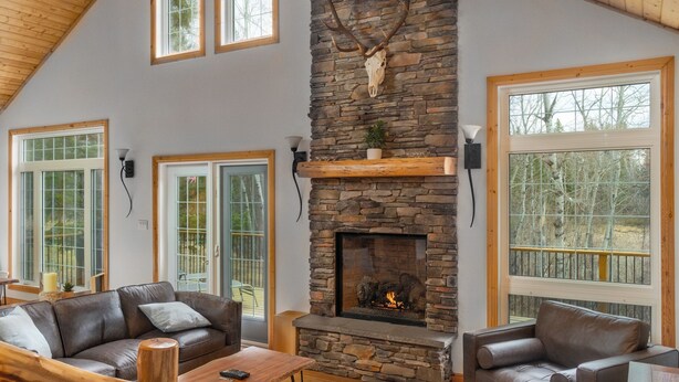 A spacious living room with a stone fireplace, leather sofas, and large windows.