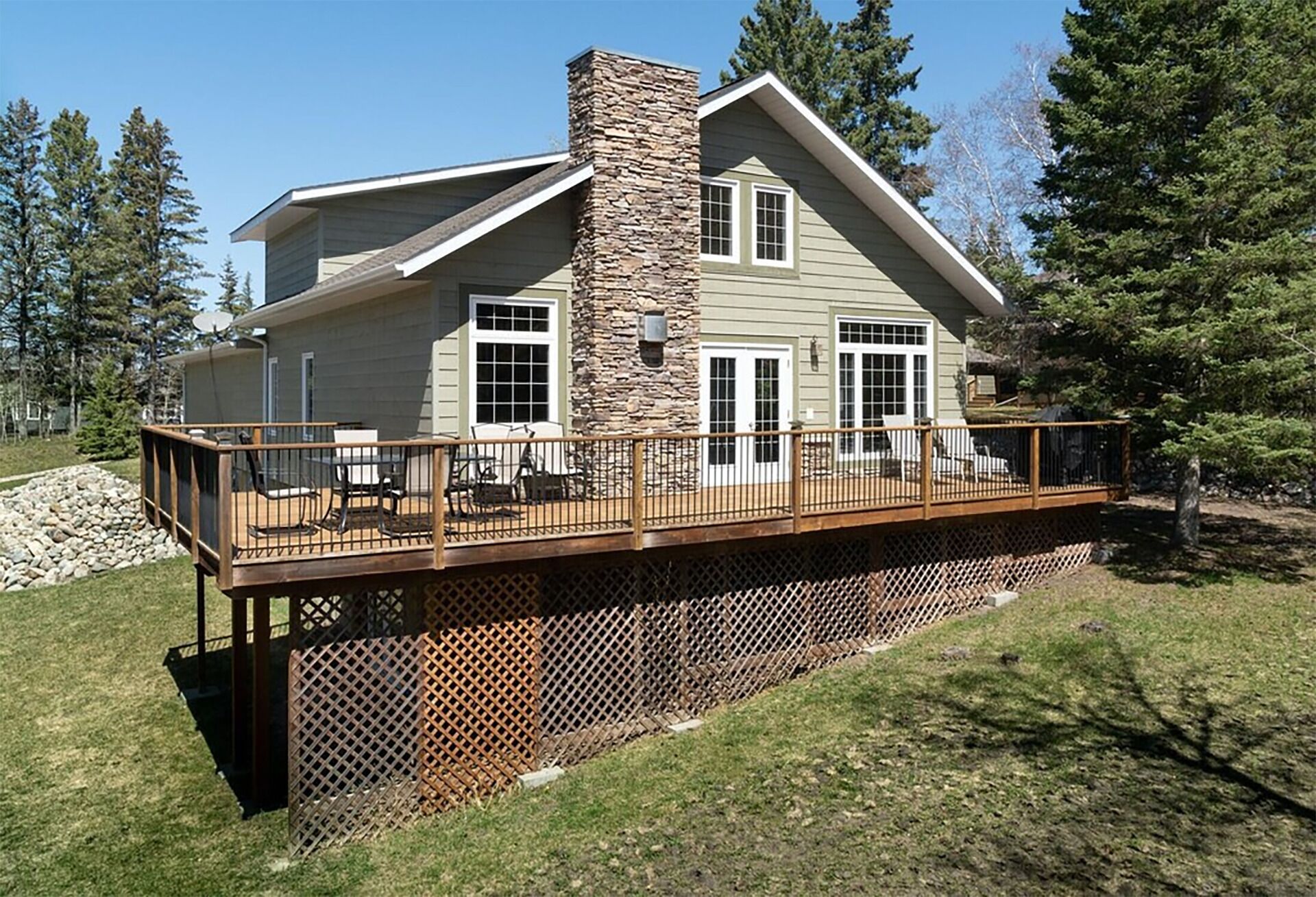 A two-story house with a stone chimney, large windows, and a wooden deck.
