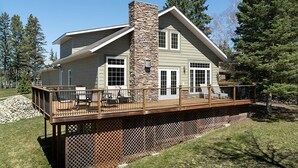 A two-story house with a stone chimney, large windows, and a wooden deck.