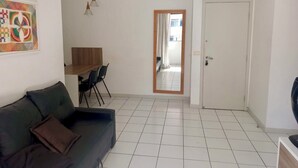 Een woonkamer met een donkere bank, een houten eettafel met twee stoelen, een witte deur en een kleurrijk abstract schilderij aan de muur.