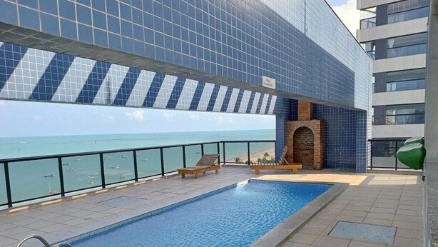 Een dakzwembad met uitzicht op zee, een houten terras en een modern gebouw met blauw betegelde muren.
