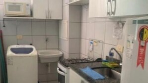 Een kleine keuken met witte kastjes, een magnetron, een spoelbak en een fornuis.