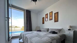Un dormitorio con una cama grande, una mesita de noche, una lámpara y vistas a una piscina a través de una puerta corrediza de vidrio.