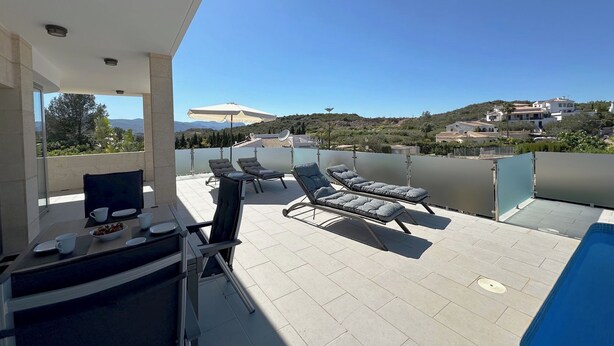 Terraza en la azotea con sillones de descanso y una piscina, con vistas a un paisaje pintoresco con casas y colinas.