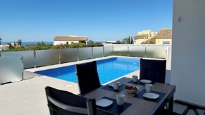 Una piscina en la azotea con vistas despejadas al mar, una mesa de comedor con sillas y vistas de edificios circundantes.