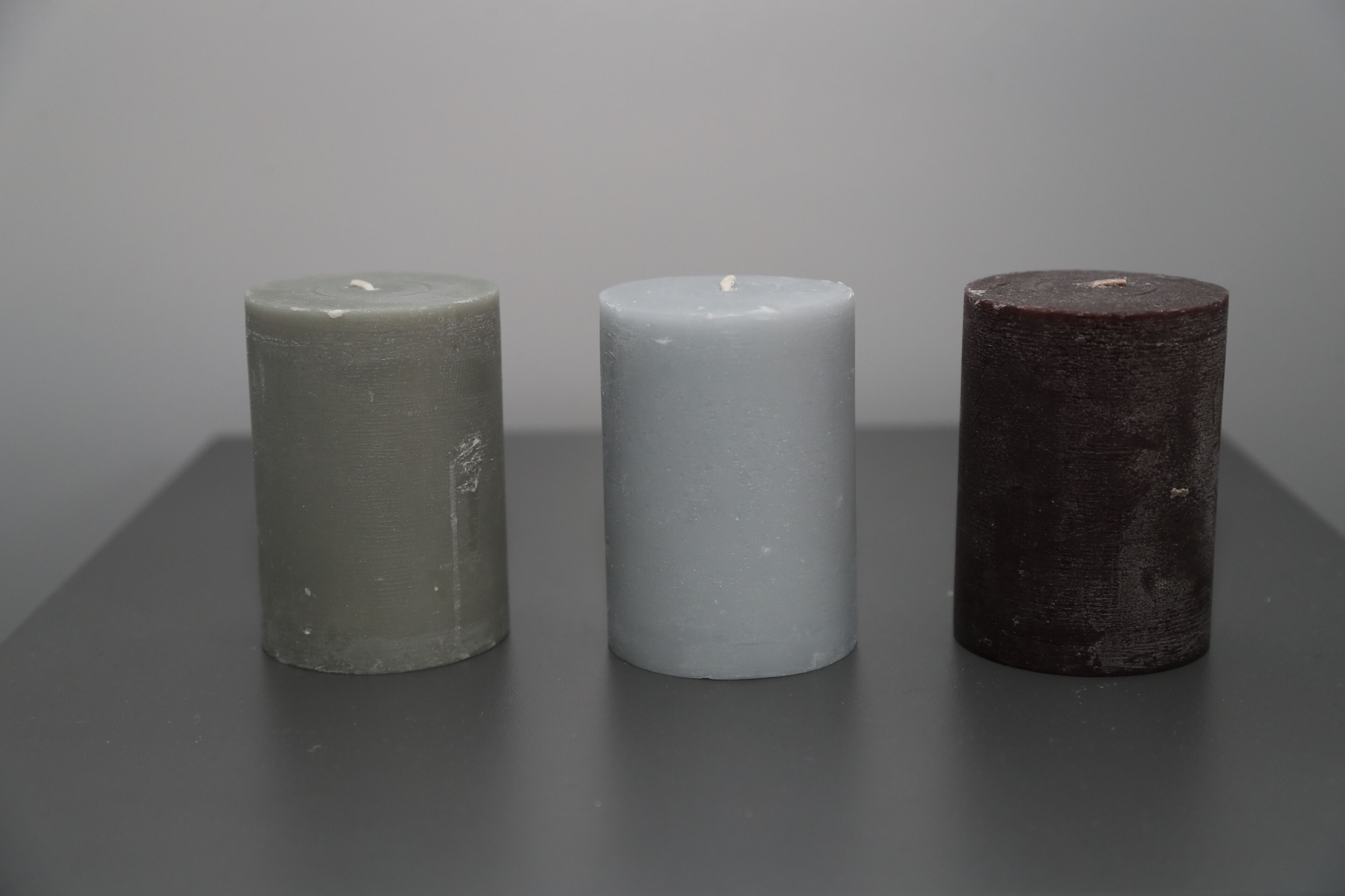 Tre candele cilindriche di colori diversi su una superficie piana.