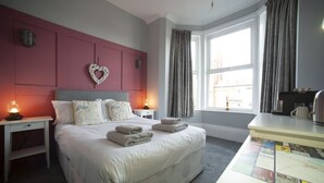 A hotel room with a large bed, bedside lamps, a heart-shaped decoration on the wall, and a view of the city through the window. - The Southport Two-Bed @ Stay Victoria Suites (Merseyside)