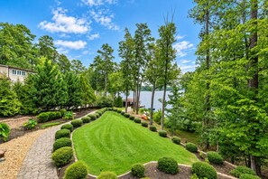 A well-maintained garden with a lawn, a variety of trees, and a body of water in the background.