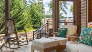 Un espace extérieur abrité avec des sièges, offrant une vue sur un lac, comprenant une chaise suspendue en bois et un banc rembourré.