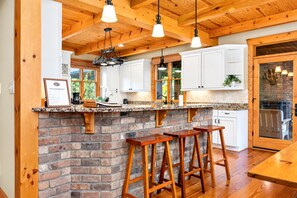 A kitchen with a brick island, wooden stools, and pendant lighting.
