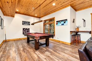 A pool table in a room with wooden flooring and a wooden ceiling.