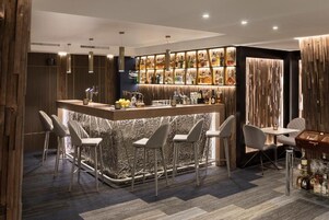 Uma área de bar moderna com balcão de pedra, banquetas e diversos tipos de garrafas.