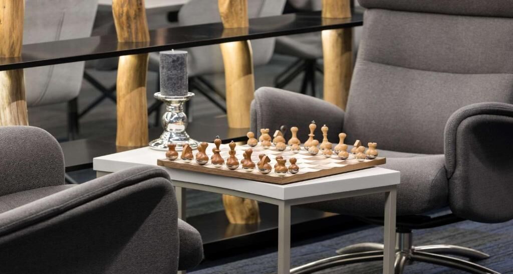 A chessboard on a table with a candle and chairs around it.