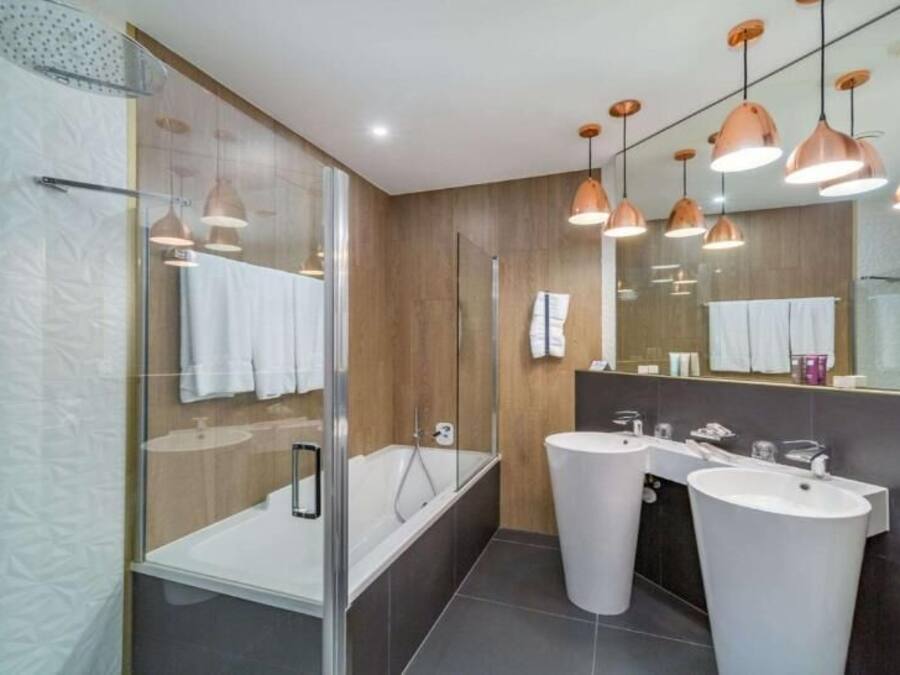 Ein modernes Badezimmer mit Glasdusche, zwei Waschbecken und Pendelleuchten.