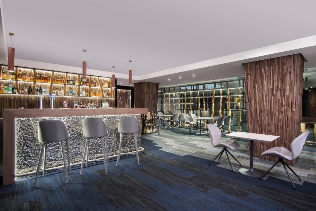 A modern bar area with a marble counter, bar stools, and a seating area with tables and chairs.